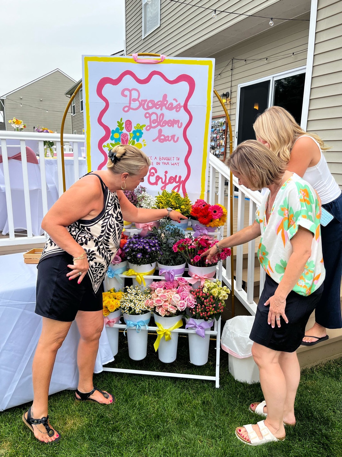 At a BBB gathering · Guests choosing bright flowers from ribboned buckets outdoors